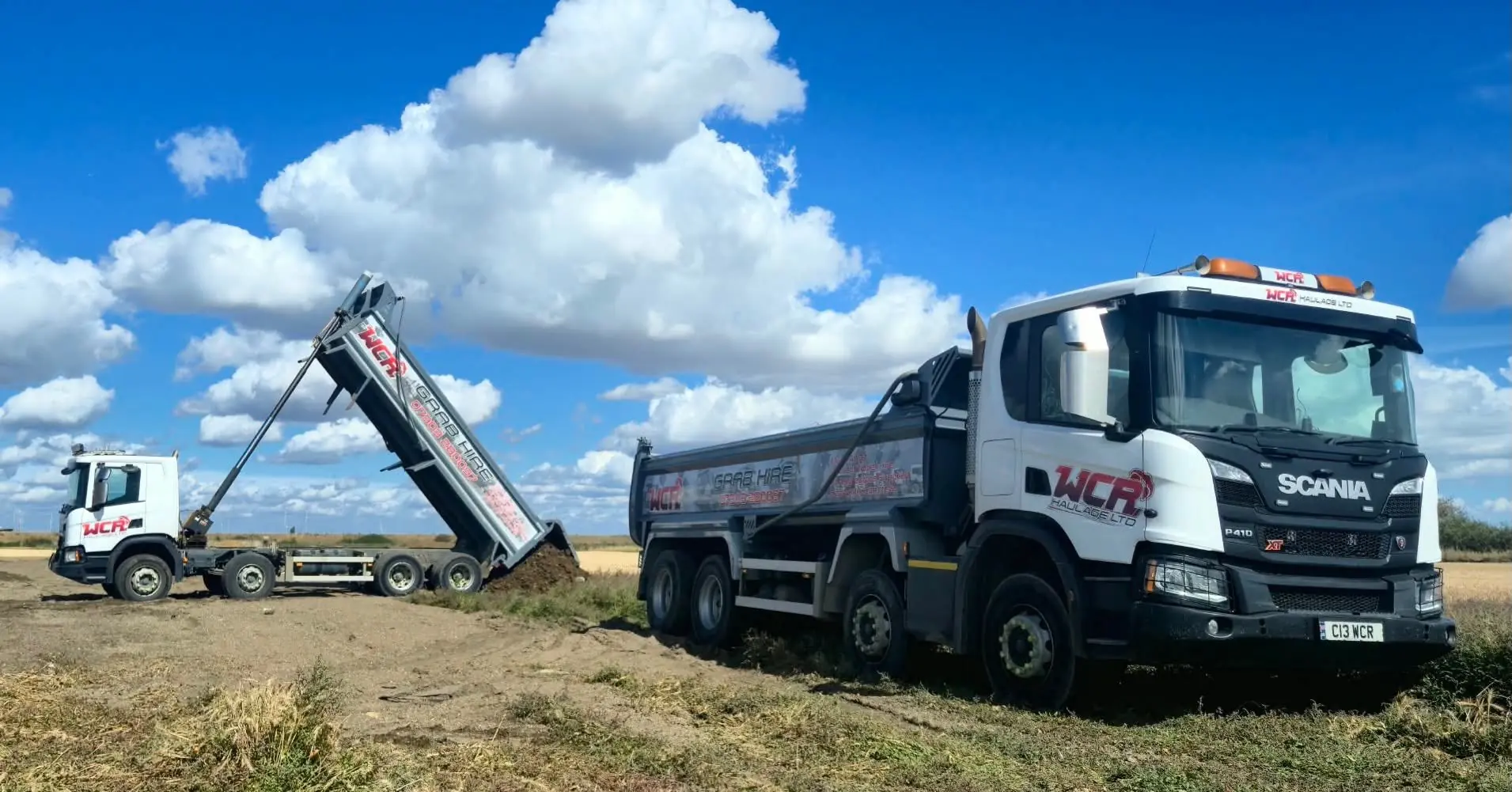 Two WCR tipper lorries on an open site, with one body raised