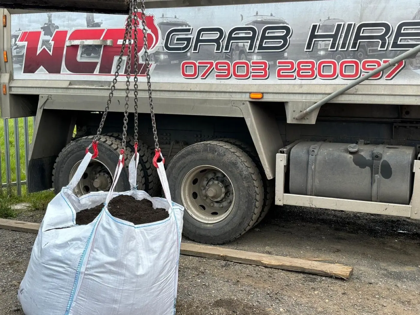 Two bulk bags of loose material suspended beside a WCR grab lorry