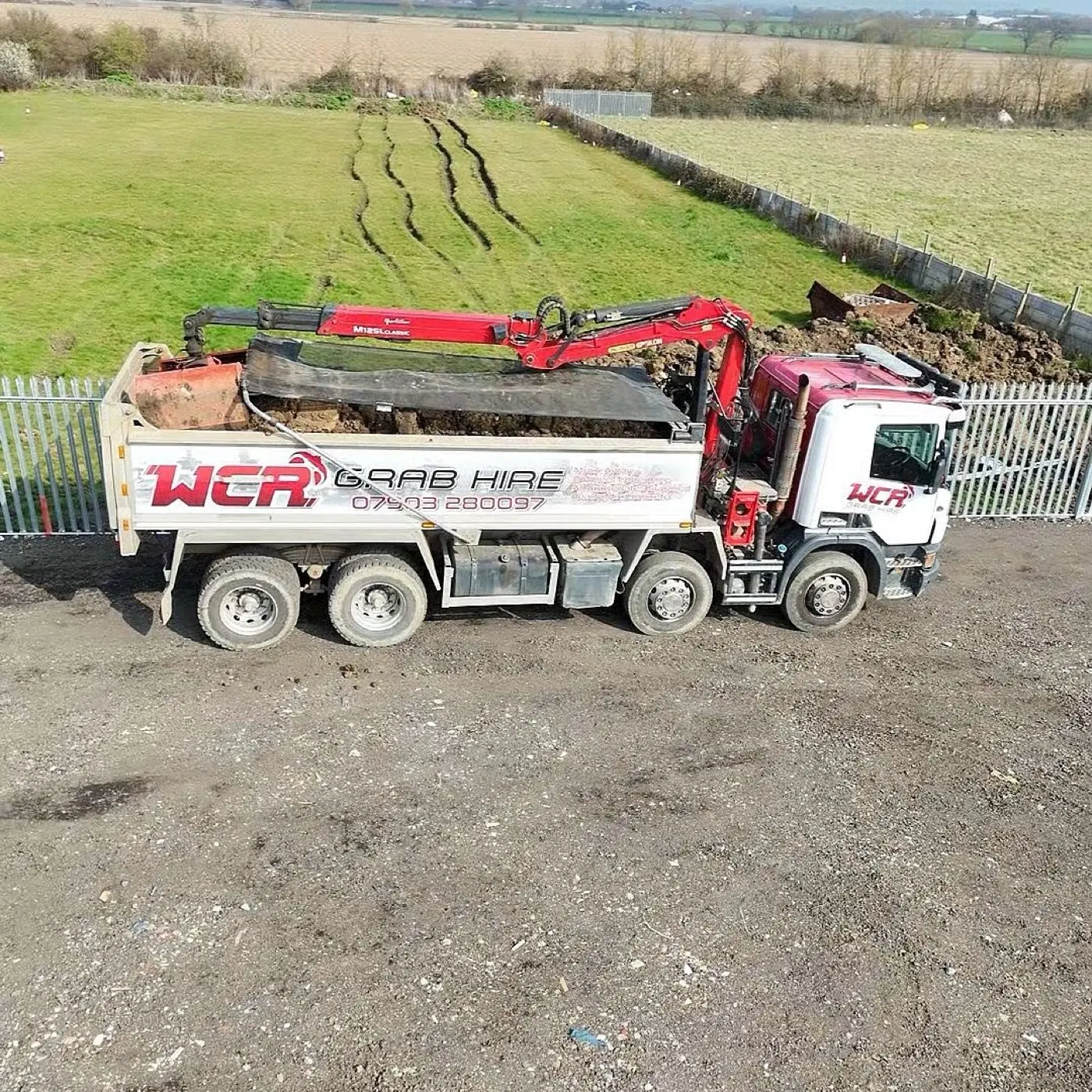 Side view from above of a WCR grab lorry beside a fenced yard