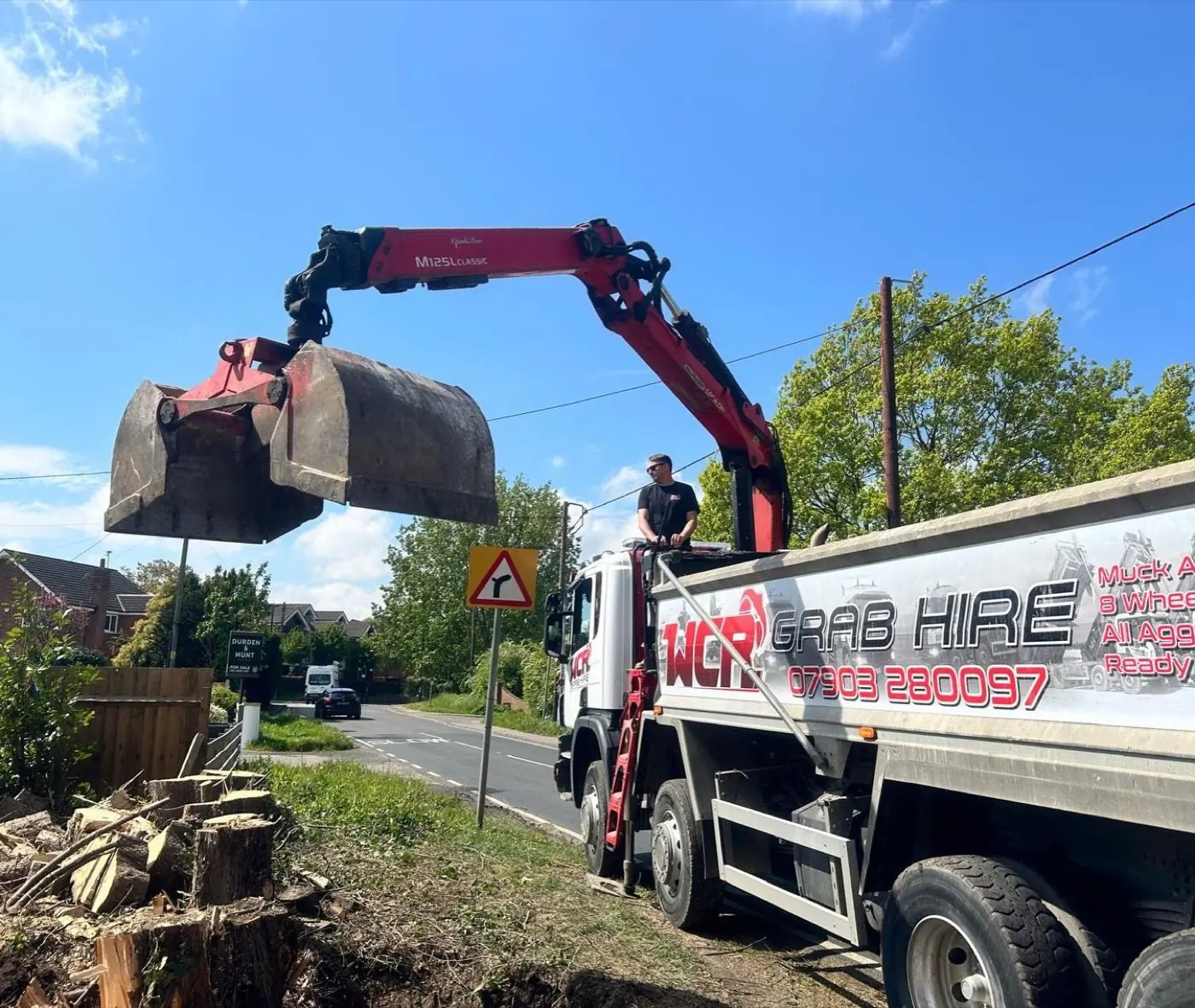 WCR grab arm extended over excavated material beside a residential road